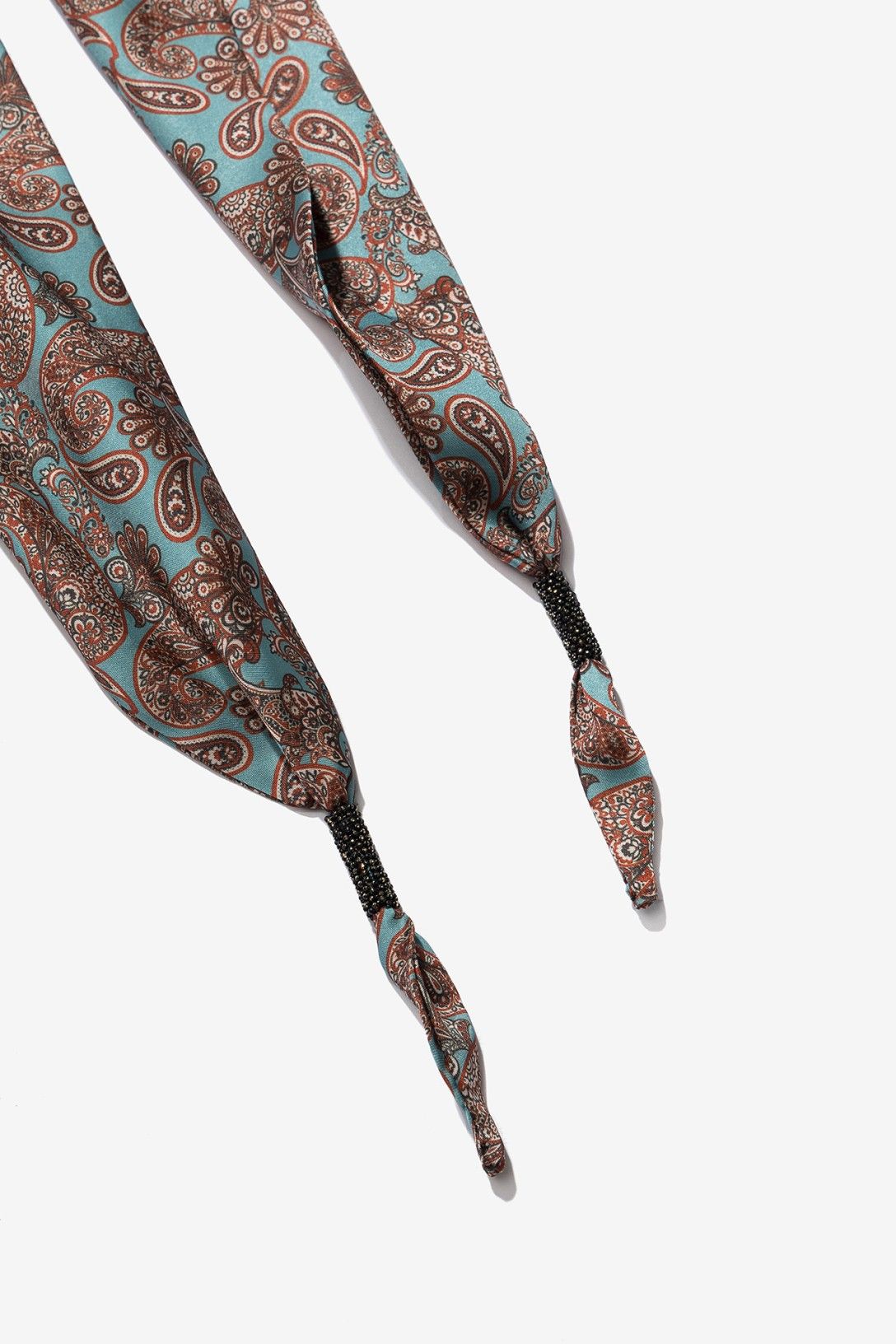 Bandana estampada paisley de Vilanova en tonos azul aguamarina y marrón con detalle decorativo de cuentas negras en los extremos.