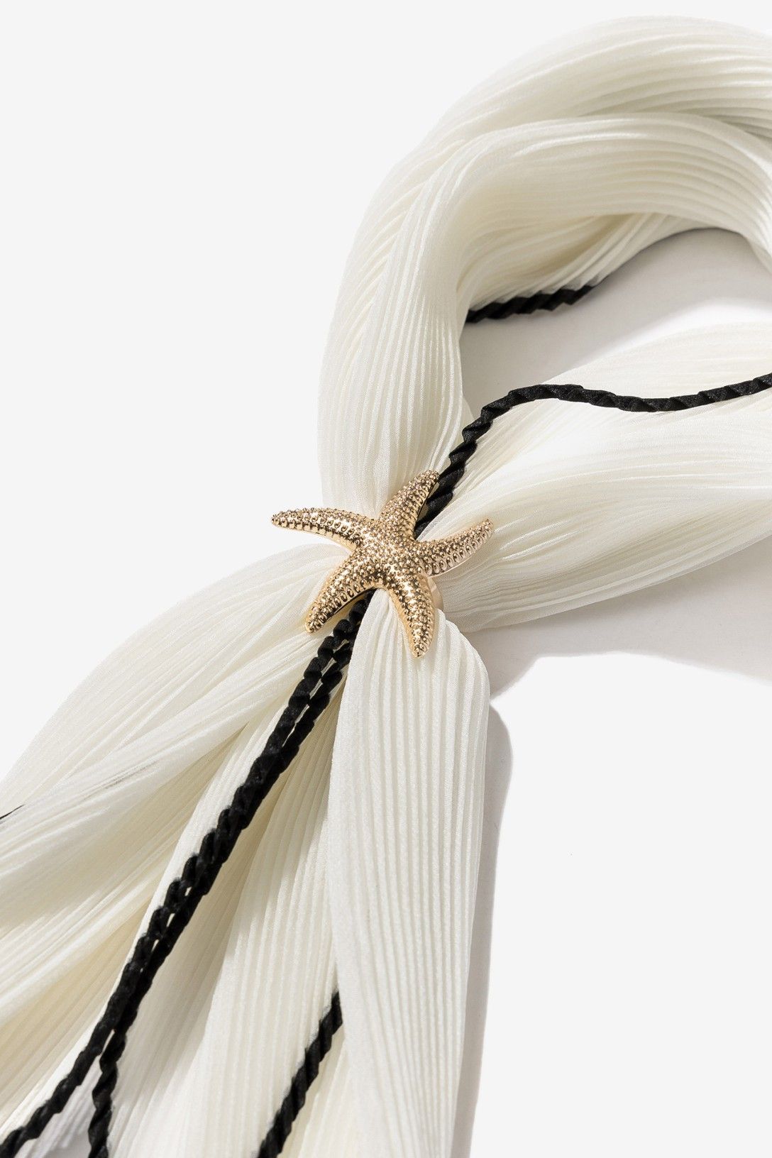Bandana plisada blanca Vilanova con ribete negro y broche dorado en forma de estrella de mar.