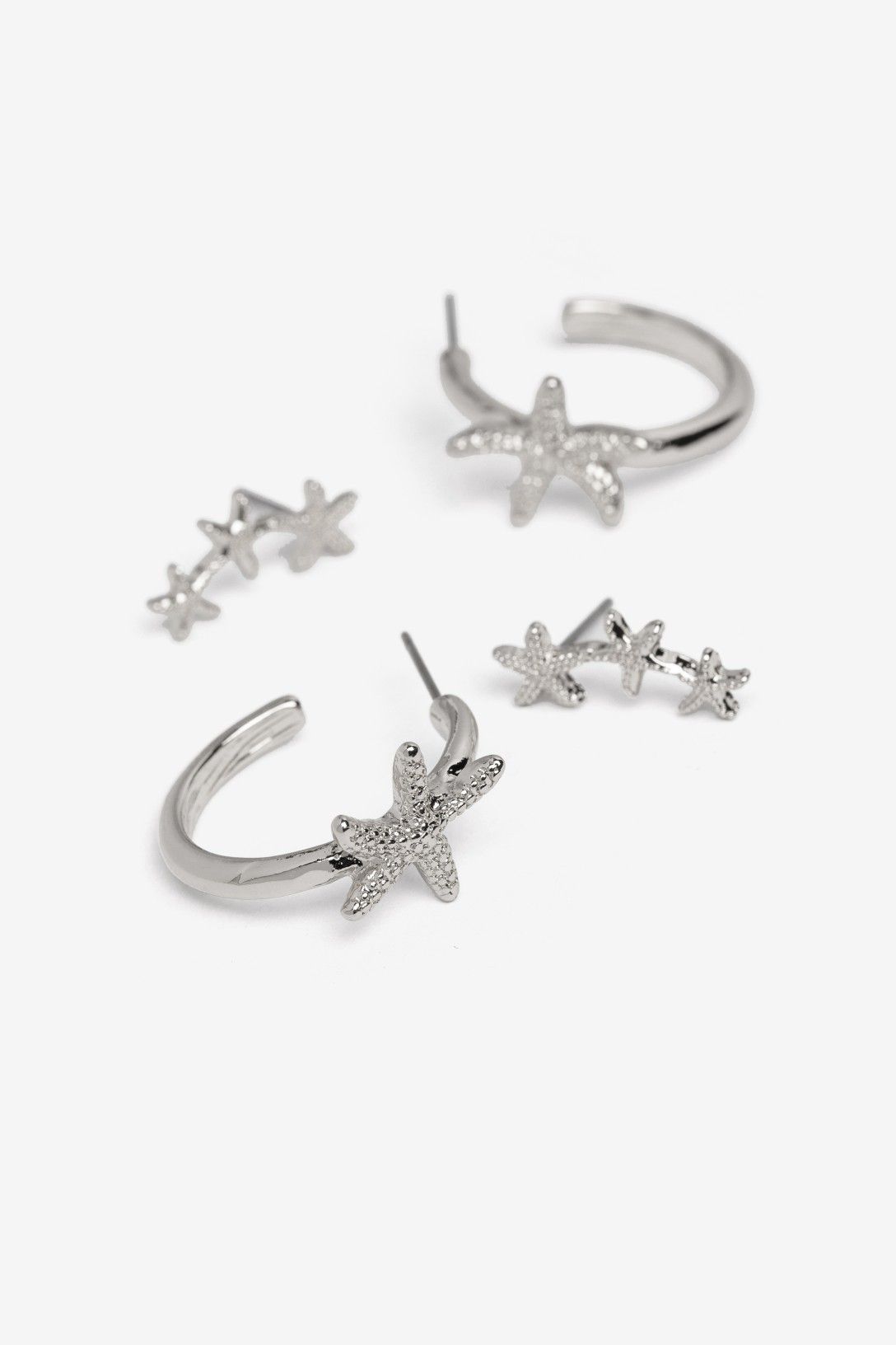 Pack de pendientes plateados Vilanova con diseño de estrellas de mar, compuesto por aros decorativos y pendientes trepadores.
